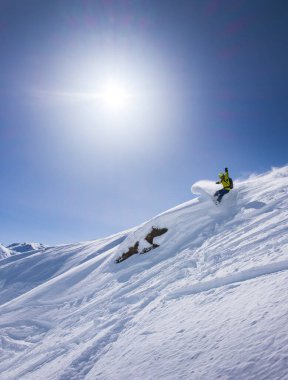 Snowboard kayaların yakınına döner, güneşte mavi gökyüzü püskürterek.