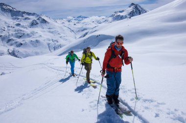 Ski touring group in the mountains of Kitzbueheler Alps at climbing the mountain peak Schafsiedl on ski from the Bamberger Hut. Three men with colourful clothes in front of the mountain scenery clipart