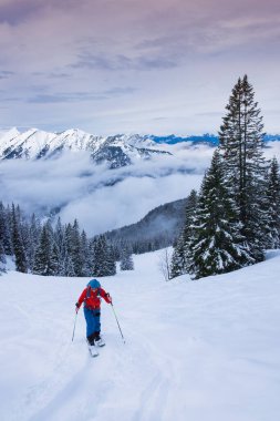 Karwendel dağlarında kayak yapan bir adam, dağ zirvesine tırmanıyor kayak yapıyor, dağ manzarasının önünde.