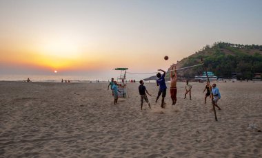02 / 19 / 2019 Gokarna, Hindistan. Kafkas ve Hintli erkekler kumsalda voleybol oynuyorlar. İnanılmaz bir gün batımı.