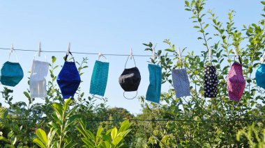 a lot of different self made corona face masks out of fabric hanging on a clothesline for drying clipart