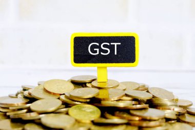 Seçici odak 'Gst' yazılı sarı yazı tahtası ile altın sikke. İş, finans ve vergi kavramı.