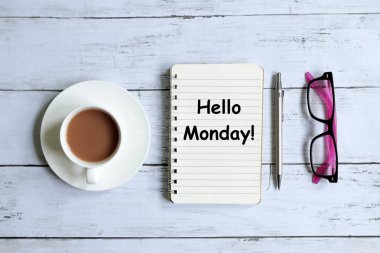 Bir fincan kahve, kalem, güneş gözlüğü ve 'Merhaba ile Pazartesi!' Beyaz ahşap arka plan üzerinde yazılı defter üstten görünüm.