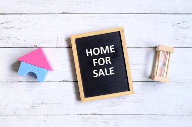 Üstten görünüm ev modeli, kum saati ve yazı tahtası 'Ev Satılık ile' Beyaz ahşap arka plan üzerinde yazılı. Emlak ve gayrimenkul Tema.