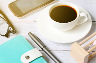 Üstten görünüm ve kum saati, güneş gözlüğü, dizüstü bilgisayar, cep telefonu ve kalem Beyaz ahşap zemin üzerinde siyah kahve bir fincan seçici odak.