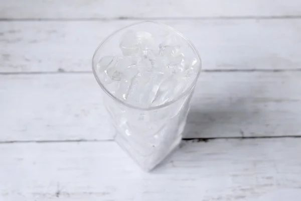 Top view of transparent glass fill with ice cube on white wooden background.