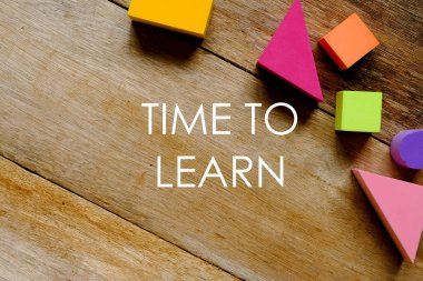 Ahşap zemin üzerinde 'Öğrenmeye Zaman' yazılı renkli yumuşak blokların üst görünümü.