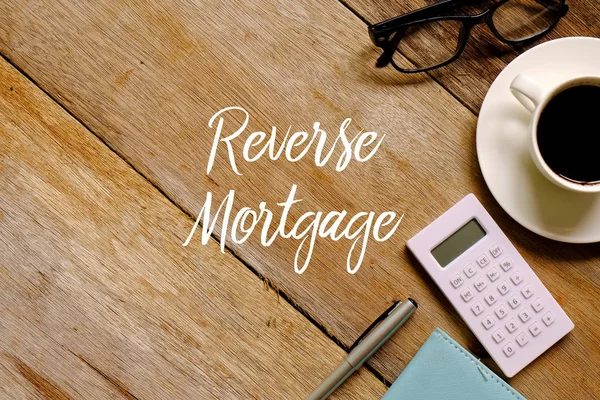 Bir fincan kahve, hesap makinesi, Gözlük, defter ve kalem ile ters ipotek yazılı ahşap arka plan üzerinde yukarıdan.