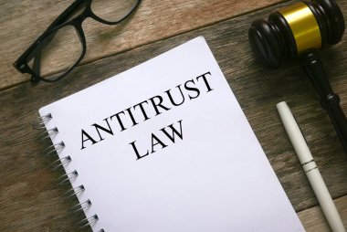 Tahta zemin üzerine anti tröst kanunu ile yazılmış bir gözlük, kalem, tokmak ve defter üst görünümü.