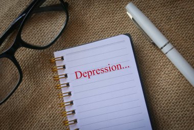 Kilim arka planında Bunalım ile yazılmış bir gözlük, kalem ve defterin üst görünümü.