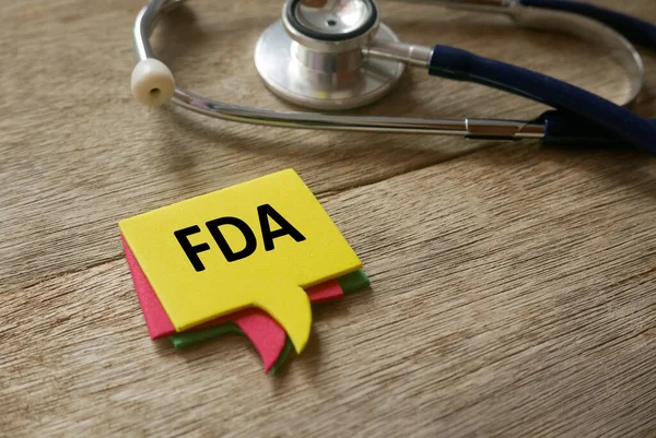 Seçici steteskop odağı ve FDA ile ahşap arka planda yazılmış renkli konuşma baloncukları.