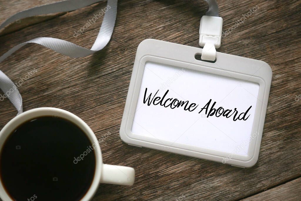 Selective focus and top view of a black coffee together with lanyard and name tag written with Welcome aboard on wooden background.