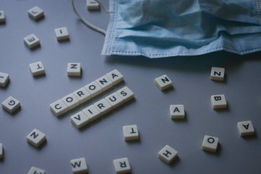 Corona Virüsü ile yazılmış, gri arkaplanda cerrahi maskeli küp alfabesi.