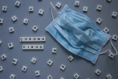 Corona Virüsü ile yazılmış, gri arkaplanda cerrahi maskeli küp alfabesi.