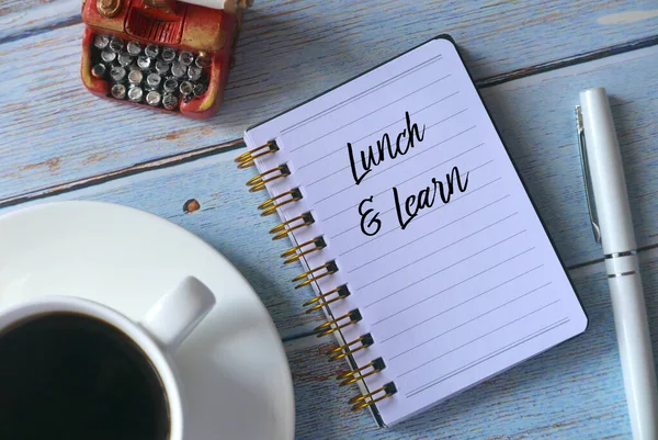 Bir fincan kahvenin üst görüntüsü, klasik oyuncak daktilo, kalem ve not defteri, Lunch and Learn ile ahşap arka planda yazılmış..