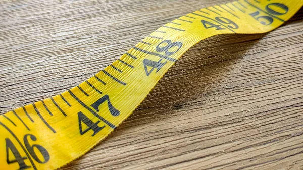 Tahta bir yüzeyde duran, inç ve ölçü işaretlerini gösteren parlak sarı bir mezura..