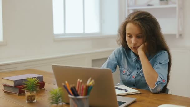 Chica joven con computadora portátil está haciendo la tarea. Educación universitaria. Mujer cansada estudiante estudiando y usando PC en casa . — Vídeo de stock