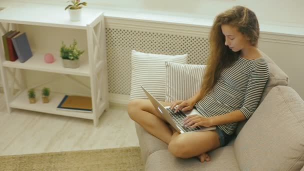 Menina adolescente feliz em um sofá usa laptop . — Vídeo de Stock