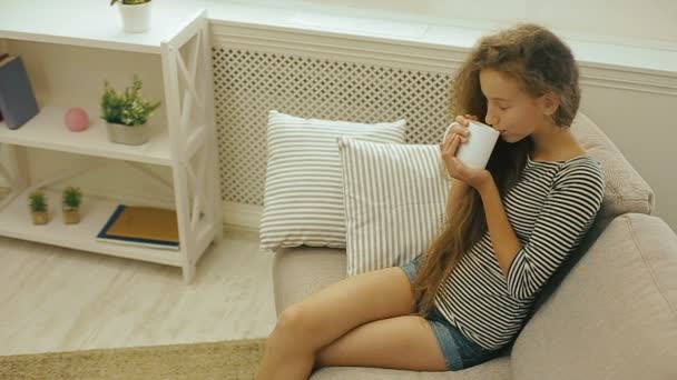 Young girl drinking fresh milk sitting on a sofa — Stock Video