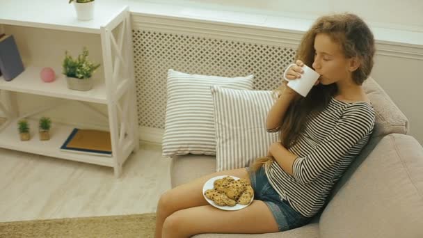 Young girl drinking fresh milk sitting on a sofa — Stock Video