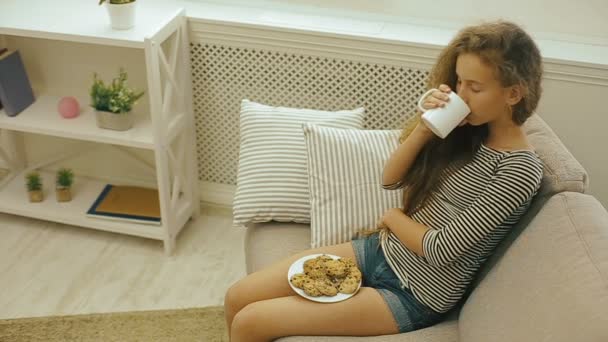 Young girl drinking fresh milk sitting on a sofa — Stock Video