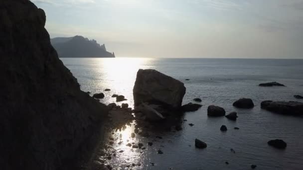 Voo sobre o mar, pedras e pedras ao nascer do sol. Montanhas, rochas, pedras na água e ondas do mar. Vista aérea da montanha Kara Dag na Crimeia . — Vídeo de Stock