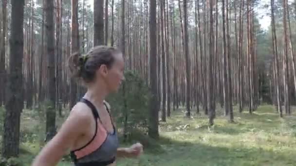 Giovane donna felice sta facendo jogging in una foresta tra gli alberi. Tracking shot con telecamera stabilizzata — Video Stock