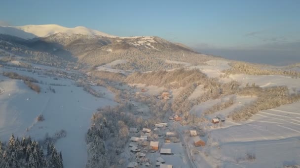 Vuelo sobre un pueblo en las montañas Cárpatas. Vista de aves de casas cubiertas de nieve en las montañas. Paisaje rural en invierno. Pueblo de los Cárpatos en la nieve desde una altura . — Vídeos de Stock