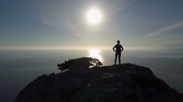 Silueta aérea de mujer joven de pie en la cima de una montaña frente al mar. Señora en la cumbre en un hermoso paisaje . — Vídeo de stock