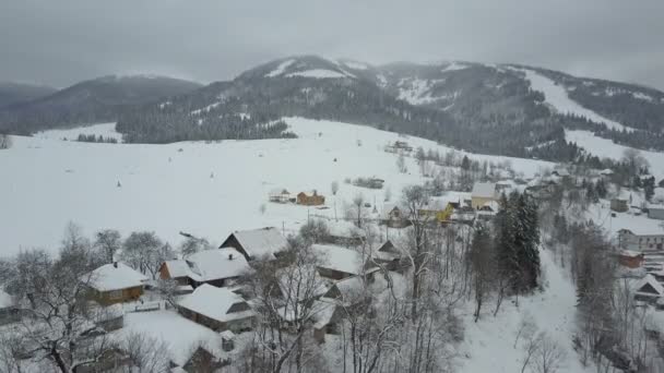 Lot nad wieś w Karpatach. Widok domów pokrytych śniegiem w górach z lotu ptaka. Wiejski krajobraz zimą. Karpackiej wsi w śniegu z wysokości. — Wideo stockowe