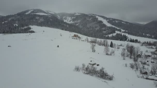 Voo sobre uma aldeia nas montanhas dos Cárpatos. Vista de olhos de pássaros de casas cobertas de neve em montanhas. Paisagem rural no inverno. Aldeia dos Cárpatos na neve de uma altura . — Vídeo de Stock