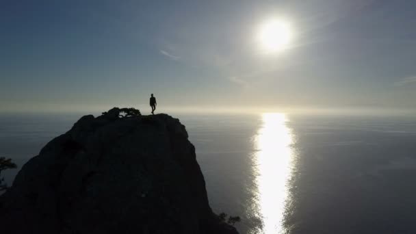 Luchtfoto silhouet van jonge vrouw lopen op de top van een berg met uitzicht op zee. Dame op de top zwaaien hand in prachtige omgeving. — Stockvideo