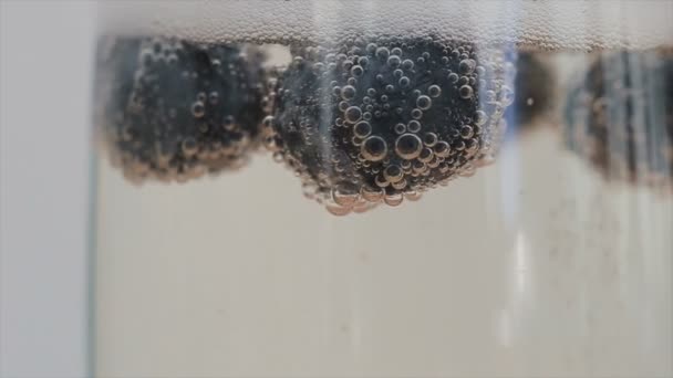 Gros plan de bulles de champagne attachées aux bleuets flottant dans un verre. Mouvement lent . — Video