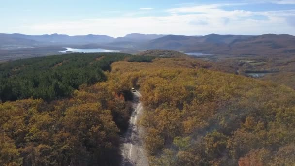 Légifelvételek autó áthajtás az erdő, a hegyek. Ősszel gyönyörű hegyi úton vezetéssel. Légi trekking lövés egy kis autó. — Stock videók