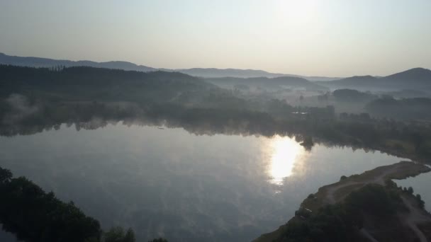 Avión cinematográfico vuela a través de una niebla matutina sobre un lago de montaña. Amanecer brumoso en las montañas . — Vídeos de Stock