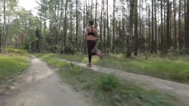 Eine glückliche junge Frau joggt in einem Wald zwischen Bäumen. Kamerafahrt mit stabilisierter Kamera — Stockvideo