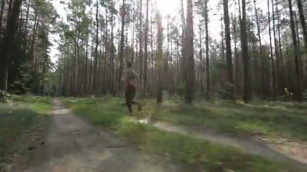 Happy young woman is jogging in a forest among trees. Tracking shot with stabilized camera — Stock Video