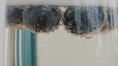 Şampanya kabarcıklar yaban mersini bir cam yüzen bağlı closeup. Ağır çekim.