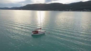 Dağlarda büyük bir gölde küçük bir yat havadan görünümü. Tekne gölde hareket ediyor. Klagenfurt Carinthia Avusturya.