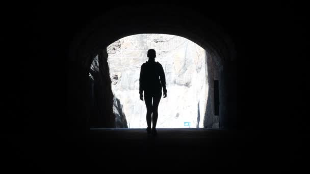Camera follows a woman silhouette walking through dark tunnel towards the light raising arms in air. — Stock Video