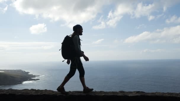 Hombre excursionista con dolor de espalda está caminando en el borde de una carretera en las islas canarias por encima del océano . — Vídeos de Stock