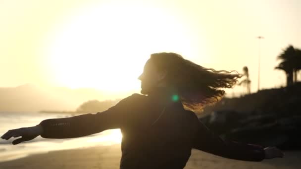 Slow Motion Fechar silhueta de Young Woman dançando em uma praia com o cabelo soprando no vento olhando para o pôr do sol sobre o oceano . — Vídeo de Stock