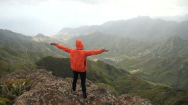 Anaga Dağları, Kanarya Adaları, Tenerife manzarası eşliğinde turuncu ceket aktif otostopçu kız. Bir dağın üstünde sırt çantası ile Hiker kadın.