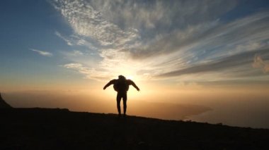 Yavaş hareket güzel gün batımı atlama iyimser bir adamın silueti. Güçlü rüzgar ceketi doldurur.