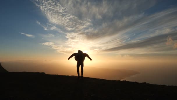 Silueta de un hombre optimista saltando a la hermosa puesta de sol en cámara lenta. El fuerte viento llena la chaqueta . — Vídeo de stock