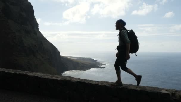 Hombre excursionista con dolor de espalda está caminando en el borde de una carretera en las islas canarias por encima del océano . — Vídeos de Stock