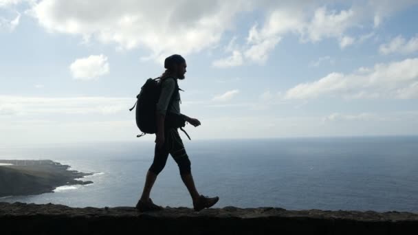 L'escursionista uomo con lo zaino sta camminando sul bordo di una strada in isole di canarino sopra l'oceano. Tenerife — Video Stock