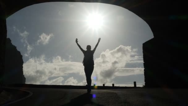 Camera volgt een vrouw silhouet lopen van tunnel naar het zonlicht. Uitbarsting van fel licht. Het verhogen van wapens in de lucht. — Stockvideo