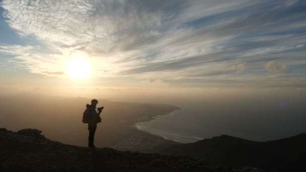 Silueta dívky v cyklistické přilbě s batohu fotografovat neuvěřitelný západ slunce na vrcholku hory nad mořem na Kanárských ostrovech. Lanzarote. — Stock video