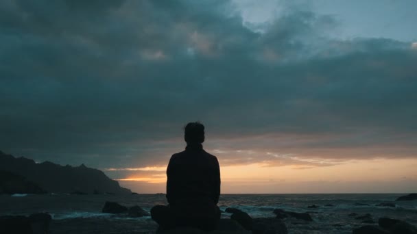 Silueta de una mujer sentada sobre rocas al atardecer observando las olas del océano en la playa de Benijo en Tenerife, Islas Canarias . — Vídeo de stock